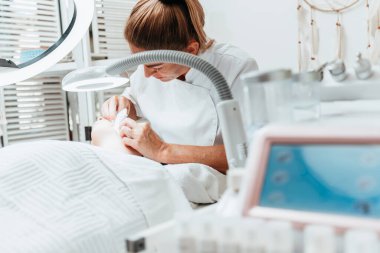 Modern donanımlı güzellik merkezinde profesyonel bir güzellik uzmanı genç bir kadının yüzündeki sivilceleri ve sivilceleri elle temizliyor. Yüz Temizleme. Güzelleştirme ve cilt sağlığı kavramı.