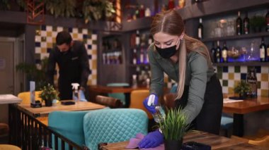 Genç restoran garsonları Coronavirus salgını sırasında masaları ve yüzeyleri temizleyip dezenfekte ediyorlar. Koruyucu maske ve eldiven takıyorlar..