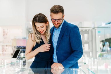 Modern kuyumcuda alışveriş yapan güzel bir çift. Genç bir kadın denesin. Muhteşem, pahalı kolye ve küpeler. Moda tarzı ve tüketim konsepti.