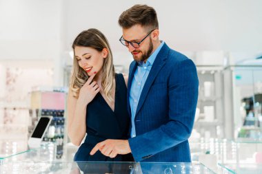 Modern kuyumcuda alışveriş yapan güzel bir çift. Genç bir kadın denesin. Muhteşem, pahalı kolye ve küpeler. Moda tarzı ve tüketim konsepti.