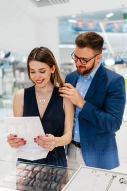 Modern kuyumcuda alışveriş yapan güzel bir çift. Genç bir kadın denesin. Muhteşem, pahalı kolye ve küpeler. Moda tarzı ve tüketim konsepti.