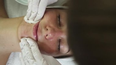 Profesyonel güzellik uzmanı genç güzel bir kadının yüzüne glikolik asit kabuğu yapıştırıyor. Kimyasal soyma ve güzellik tedavi konsepti.