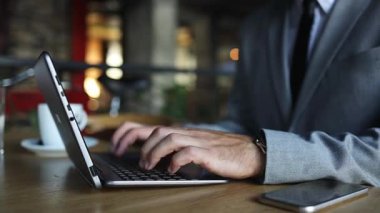 Restoranda ya da kafe barda oturan yakışıklı bir iş adamı ve iş için dizüstü bilgisayarını ve akıllı telefonunu kullanıyor..