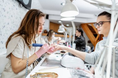 Modern bir güzellik salonunda çalışan profesyonel manikürcüler. Tatmin olmuş kadın müşteriler kaplıca merkezinde manikür tedavisi görüyor..