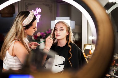 Profesyonel güzellik uzmanı güzel genç bir kadının yüzüne makyaj yapıyor. Muhteşem bir kadın modelle profesyonel makyaj stüdyosu çalışması..