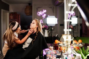 Profesyonel güzellik uzmanı güzel genç bir kadının yüzüne makyaj yapıyor. Muhteşem bir kadın modelle profesyonel makyaj stüdyosu çalışması..