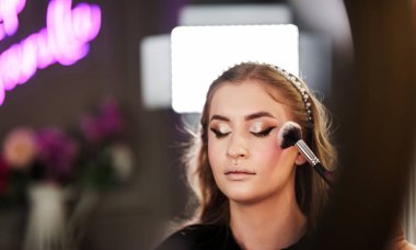 Profesyonel güzellik uzmanı güzel genç bir kadının yüzüne makyaj yapıyor. Muhteşem bir kadın modelle profesyonel makyaj stüdyosu çalışması..