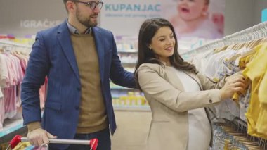 Çekici, orta yaşlı bir çift yeni bebekleri için elbise ve eşyalar almaktan zevk alıyor. Bebek dükkanında ya da dükkanda güzel bir çift. Bebek konsepti bekleniyor..