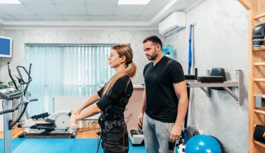 Profesyonel fizyoterapist, EMS giysili güzel bir bayanla özel elektro uyarı eğitimi ya da tedavisi sırasında çalışıyor. Modern ve parlak bir stüdyo.
