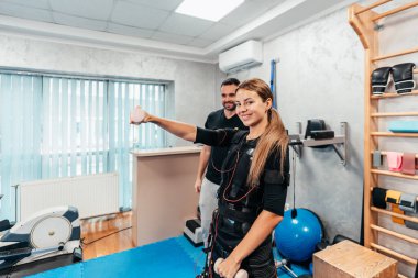 Profesyonel fizyoterapist, EMS giysili güzel bir bayanla özel elektro uyarı eğitimi ya da tedavisi sırasında çalışıyor. Modern ve parlak bir stüdyo.