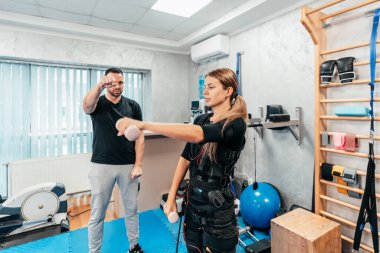 Profesyonel fizyoterapist, EMS giysili güzel bir bayanla özel elektro uyarı eğitimi ya da tedavisi sırasında çalışıyor. Modern ve parlak bir stüdyo.
