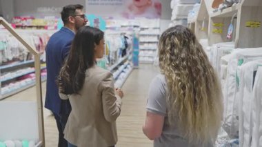Çekici orta yaşlı çift yeni bebekleri için kıyafet ve alet almaktan zevk alıyor. Yardım etmeye çalışan deneyimli bir satıcı. Bebek konsepti bekleniyor..