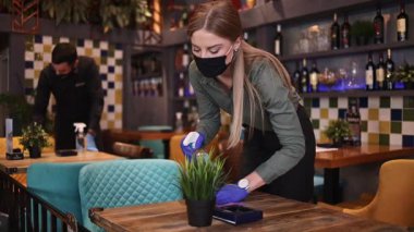 Genç restoran garsonları Coronavirus salgını sırasında masaları ve yüzeyleri temizleyip dezenfekte ediyorlar. Koruyucu maske ve eldiven takıyorlar..