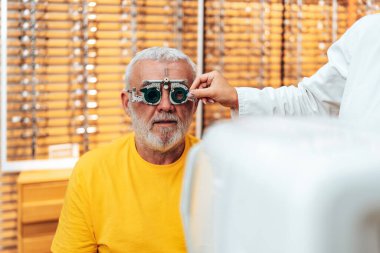 Positive senior male patient checking vision at modern ophthalmology clinic with optical trial frames.