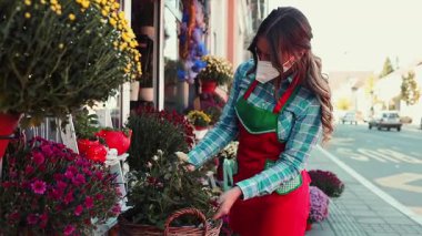Şehirde çiçekçide ya da çiçekçide çalışan genç bir kadın. Covid-19 virüs salgını sırasında koruyucu yüz maskesi takıyor. Küçük işletme kavramı.