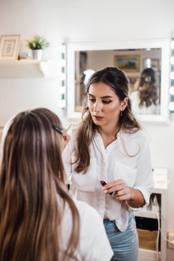 Profesyonel güzellik uzmanı güzel genç bir kadının yüzüne makyaj yapıyor. Muhteşem bir kadın modelle profesyonel makyaj stüdyosu çalışması..