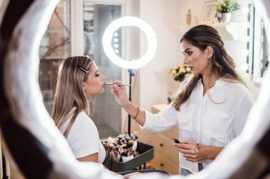 Profesyonel güzellik uzmanı güzel genç bir kadının yüzüne makyaj yapıyor. Muhteşem bir kadın modelle profesyonel makyaj stüdyosu çalışması..