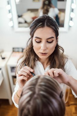 Profesyonel güzellik uzmanı güzel genç bir kadının yüzüne makyaj yapıyor. Muhteşem bir kadın modelle profesyonel makyaj stüdyosu çalışması..