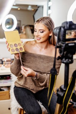 Güzel bayan çevrimiçi içerik kozmetikçisi makyaj yapıyor ve izleyicilere bazı iş araçlarını açıklıyor. Günlük kaydı ve çevrimiçi kanal çalışması. 