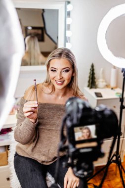 Güzel bayan çevrimiçi içerik kozmetikçisi makyaj yapıyor ve izleyicilere bazı iş araçlarını açıklıyor. Günlük kaydı ve çevrimiçi kanal çalışması. 