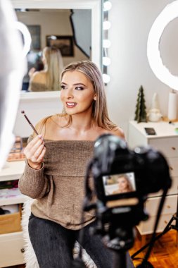 Güzel bayan çevrimiçi içerik kozmetikçisi makyaj yapıyor ve izleyicilere bazı iş araçlarını açıklıyor. Günlük kaydı ve çevrimiçi kanal çalışması. 