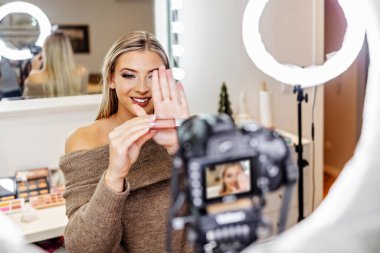 Güzel bayan çevrimiçi içerik kozmetikçisi makyaj yapıyor ve izleyicilere bazı iş araçlarını açıklıyor. Günlük kaydı ve çevrimiçi kanal çalışması. 