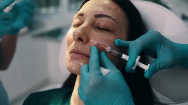 Çekici genç bir kadın güzellik kliniğinde gençleştirici yüz enjeksiyonu yaptırıyor. Güzellik uzmanı kadın kırışıklıklarını botulinyum toksin iğneleriyle ya da hyaluronik asit doldurucularıyla dolduruyor..