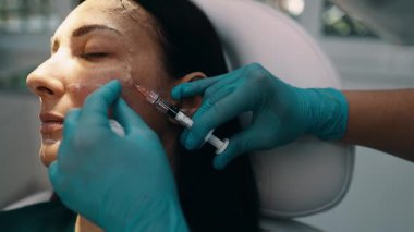 Çekici genç bir kadın güzellik kliniğinde gençleştirici yüz enjeksiyonu yaptırıyor. Güzellik uzmanı kadın kırışıklıklarını botulinyum toksin iğneleriyle ya da hyaluronik asit doldurucularıyla dolduruyor..