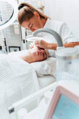Modern donanımlı güzellik merkezinde profesyonel bir güzellik uzmanı genç bir kadının yüzündeki sivilceleri ve sivilceleri elle temizliyor. Yüz Temizleme. Güzelleştirme ve cilt sağlığı kavramı.