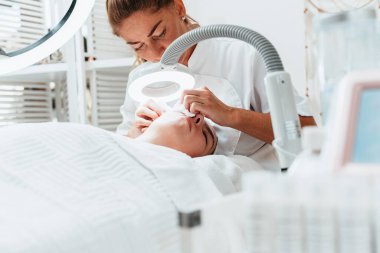 Modern donanımlı güzellik merkezinde profesyonel bir güzellik uzmanı genç bir kadının yüzündeki sivilceleri ve sivilceleri elle temizliyor. Yüz Temizleme. Güzelleştirme ve cilt sağlığı kavramı.