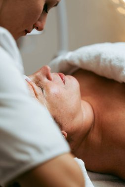 Kadın müşterinin yüzüne güzellik maskesi takan profesyonel bir kozmetikçi. Orta yaşlı kadın güzellik merkezinde ya da güzellik salonunda cilt bakımı görüyor.