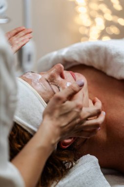 Kadın müşterinin yüzüne güzellik maskesi takan profesyonel bir kozmetikçi. Orta yaşlı kadın güzellik merkezinde ya da güzellik salonunda cilt bakımı görüyor.