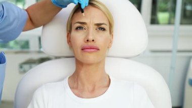 Çekici genç bir kadın güzellik kliniğinde gençleştirici yüz enjeksiyonu yaptırıyor. Güzellik uzmanı kadın kırışıklıklarını botulinyum toksin iğneleriyle ya da hyaluronik asit doldurucularıyla dolduruyor..