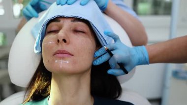 Çekici genç bir kadın güzellik kliniğinde gençleştirici yüz enjeksiyonu yaptırıyor. Güzellik uzmanı kadın kırışıklıklarını botulinyum toksin iğneleriyle ya da hyaluronik asit doldurucularıyla dolduruyor..