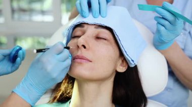 Çekici genç bir kadın güzellik kliniğinde gençleştirici yüz enjeksiyonu yaptırıyor. Güzellik uzmanı kadın kırışıklıklarını botulinyum toksin iğneleriyle ya da hyaluronik asit doldurucularıyla dolduruyor..