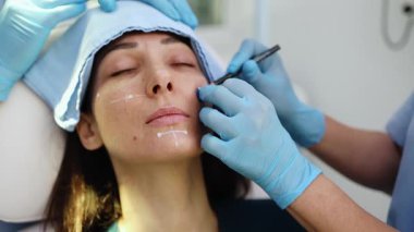 Çekici genç bir kadın güzellik kliniğinde gençleştirici yüz enjeksiyonu yaptırıyor. Güzellik uzmanı kadın kırışıklıklarını botulinyum toksin iğneleriyle ya da hyaluronik asit doldurucularıyla dolduruyor..