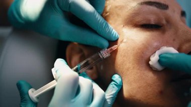Çekici genç bir kadın güzellik kliniğinde gençleştirici yüz enjeksiyonu yaptırıyor. Güzellik uzmanı kadın kırışıklıklarını botulinyum toksin iğneleriyle ya da hyaluronik asit doldurucularıyla dolduruyor..