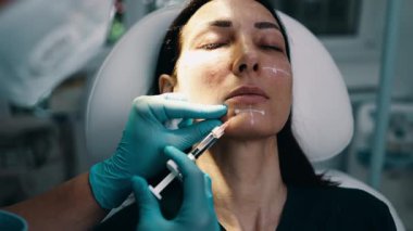 Çekici genç bir kadın güzellik kliniğinde gençleştirici yüz enjeksiyonu yaptırıyor. Güzellik uzmanı kadın kırışıklıklarını botulinyum toksin iğneleriyle ya da hyaluronik asit doldurucularıyla dolduruyor..