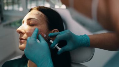 Çekici genç bir kadın güzellik kliniğinde gençleştirici yüz enjeksiyonu yaptırıyor. Güzellik uzmanı kadın kırışıklıklarını botulinyum toksin iğneleriyle ya da hyaluronik asit doldurucularıyla dolduruyor..