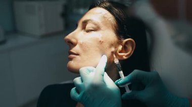 Çekici genç bir kadın güzellik kliniğinde gençleştirici yüz enjeksiyonu yaptırıyor. Güzellik uzmanı kadın kırışıklıklarını botulinyum toksin iğneleriyle ya da hyaluronik asit doldurucularıyla dolduruyor..