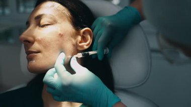 Çekici genç bir kadın güzellik kliniğinde gençleştirici yüz enjeksiyonu yaptırıyor. Güzellik uzmanı kadın kırışıklıklarını botulinyum toksin iğneleriyle ya da hyaluronik asit doldurucularıyla dolduruyor..