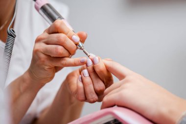 Profesyonel manikürcü ya da kuaför müşteri tırnağına oje sürerken tırnak törpüsü kullanıyor. Yakın çekim. Yüzeyin derinliği. Modern güzellik SPA ve kozmetik konsepti.