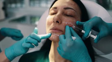 Çekici genç bir kadın güzellik kliniğinde gençleştirici yüz enjeksiyonu yaptırıyor. Güzellik uzmanı kadın kırışıklıklarını botulinyum toksin iğneleriyle ya da hyaluronik asit doldurucularıyla dolduruyor..