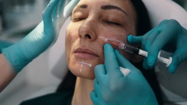 Çekici genç bir kadın güzellik kliniğinde gençleştirici yüz enjeksiyonu yaptırıyor. Güzellik uzmanı kadın kırışıklıklarını botulinyum toksin iğneleriyle ya da hyaluronik asit doldurucularıyla dolduruyor..