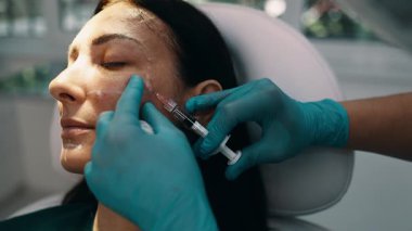 Çekici genç bir kadın güzellik kliniğinde gençleştirici yüz enjeksiyonu yaptırıyor. Güzellik uzmanı kadın kırışıklıklarını botulinyum toksin iğneleriyle ya da hyaluronik asit doldurucularıyla dolduruyor..