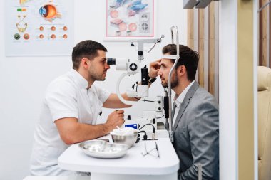 Tam donanımlı bir göz hekimi kliniğinde bir erkek hastaya göz tedavisiyle doğru teşhisi koyan bir göz muayenesi yaparken phoropter kullanan bir oftalmolog.