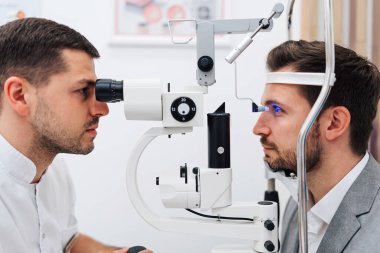 Tam donanımlı bir göz hekimi kliniğinde bir erkek hastaya göz tedavisiyle doğru teşhisi koyan bir göz muayenesi yaparken phoropter kullanan bir oftalmolog.