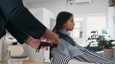 Profesyonel kuaför, kuaförde genç bir kızın ıslak saçlarını tarıyor, saç bakımına odaklanıyor ve modern çağda çocuklar için şık bir saç stili oluşturuyor.