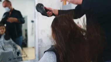 Profesyonel kuaför güzel bir kızın uzun kahverengi saçlarını ustalıkla kuruturken aynı zamanda canlı bir güzellik salonunda uzman saç bakım hizmeti veriyor.