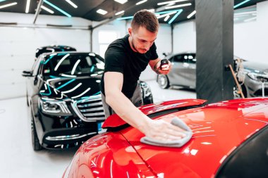 Profesyonel araba temizleyicisi kırmızı bir arabanın kaputunu cilalamak için yörünge cilası kullanıyor. Modern bir oto tamirhanesinde pürüzsüz ve parlak bir son sağlıyor.